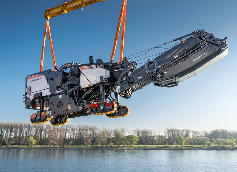 Eine Spezialbaumaschine schwebt während der Verladung an einem Kran über dem Wasser