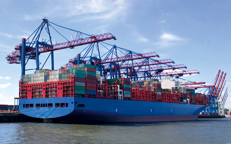 Com-16-German-Ports-Drei-Stufenplan_-c-Dakosy_4C_800px Containerschiff mit blauem Rumpf bei der Beladung, im Hintergrund sind die Containerkräne zu sehen.