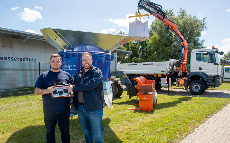 Zwei Personen die einen Lkw mit Drei-Seiten-Kipperaufbau und integriertem Ladekran präsentieren
