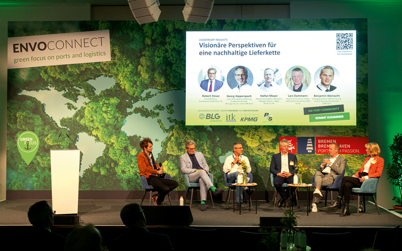 Favorit-mit-Howe-Envoconnect-2024_ENV052----c---bremenports_4C_800 Sechs Personen sitzen im Halbkreis nebeneinander auf einer Bühne bei einer Podiumsdiskussion.