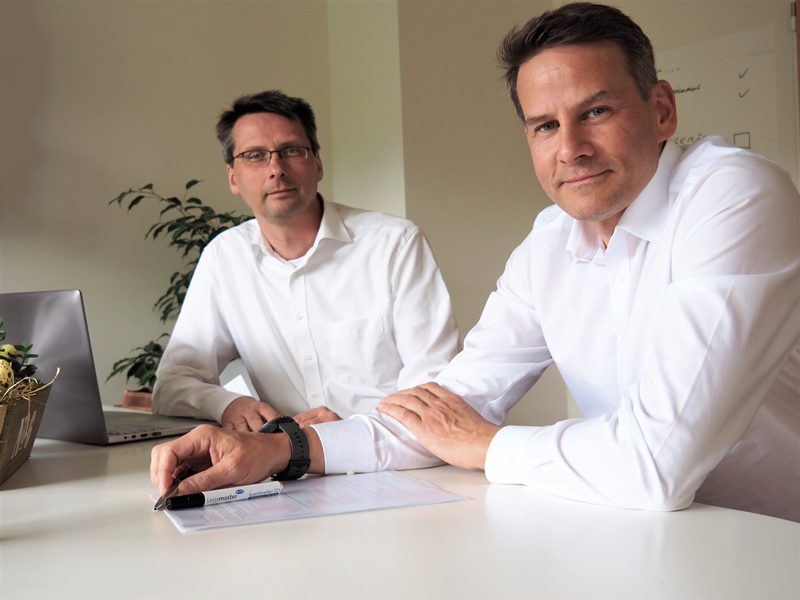 Heiko Müller und Olaf Beckedorf sitzen an einem Tisch im Büro