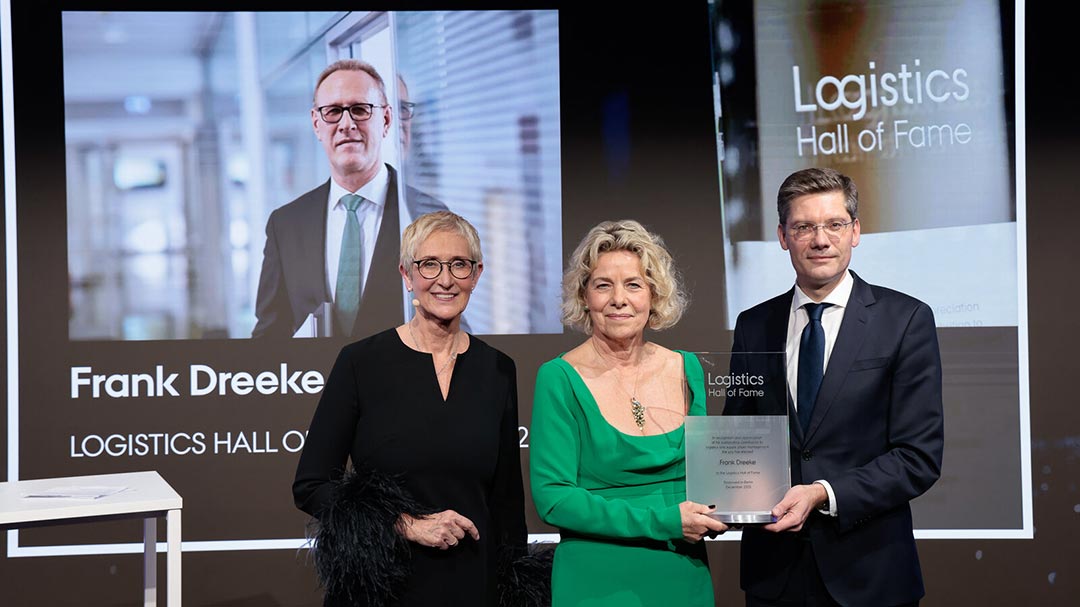Frank Dreeke’s wife, Bettina Dreeke, stands at the center of the stage as she accepts the award. The prize is presented to her by Christian Hirte, while Anita Würmser, Managing Chair of the Jury of the Logistics Hall of Fame, stands beside her. In the background, an image of her husband is shown on a screen.