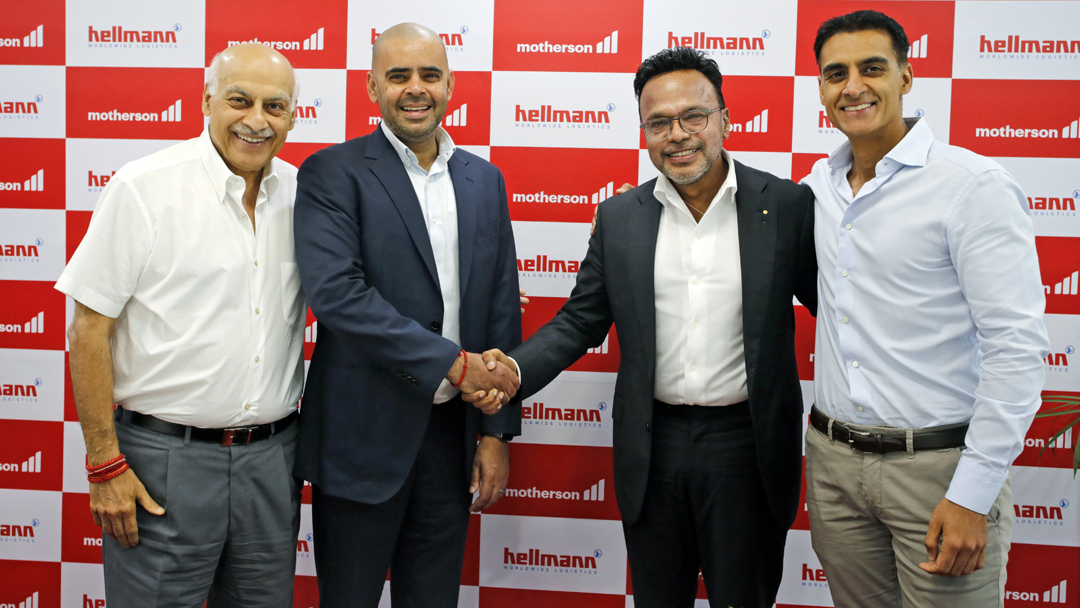 Vier Personen vor einer Wand mit Hellmann und Motherson -Logos, die Herren in der Bitte reichen sich die Hände.