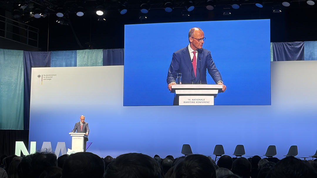 Chancellor Friedrich Merz is giving a speech on the podium; a close-up of him is visible on a screen behind him