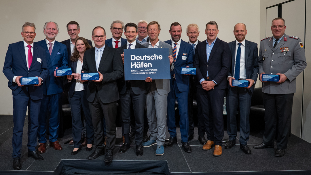 Gruppenbild mit vierzehn Personen, die Personen in der Mitte halten ein Schld mit dem Text "deutsche Häfen - eine Allianz Deutscher See- und Binnenhäfen"