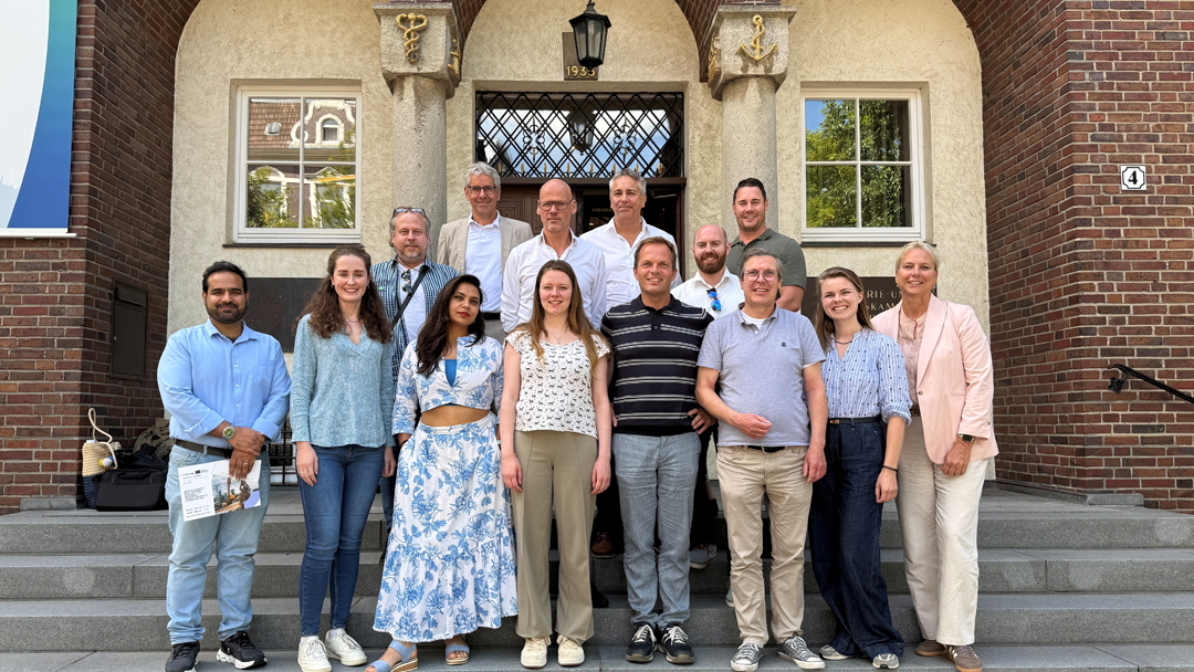 Gruppenfoto mit 14 Personen auf einer Treppe vor einem historischen Backsteingebäude