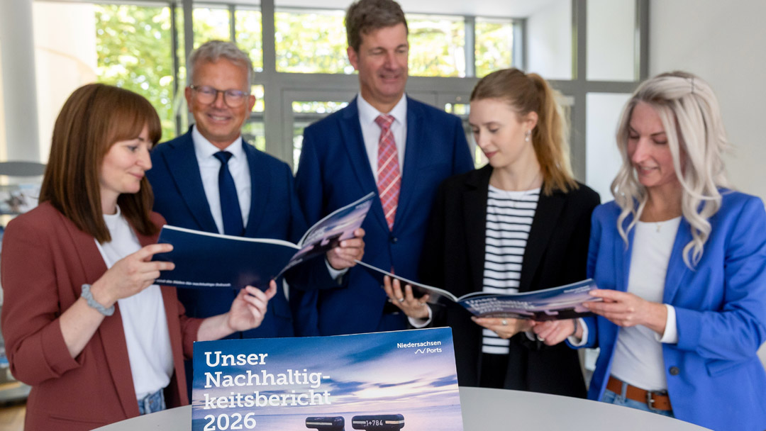 Gruppenfoto von fünf Personen, alle blicken in ein aufgeschlagenes HEft, im Vordergrund der Nachhaltigkeitsbericht.