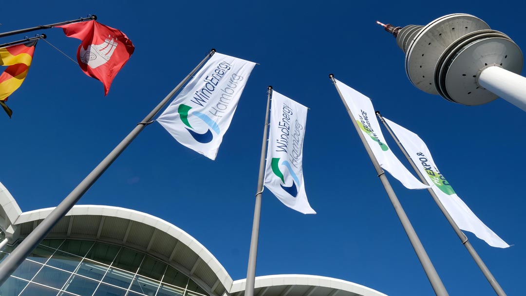 Flags at WindEnergy photographed from below; to the right of them is the television tower; the sky is deep blue