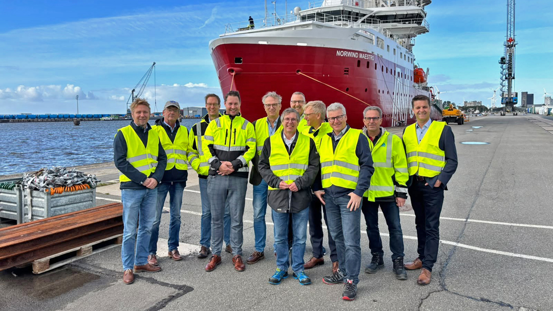 Elf Herren in gelben Warnwesten stehen an der Kaikante, im HIntergrund ein rotes Schiff, die Nordwind Maestro. Alle sehen recht vergnügt aus.