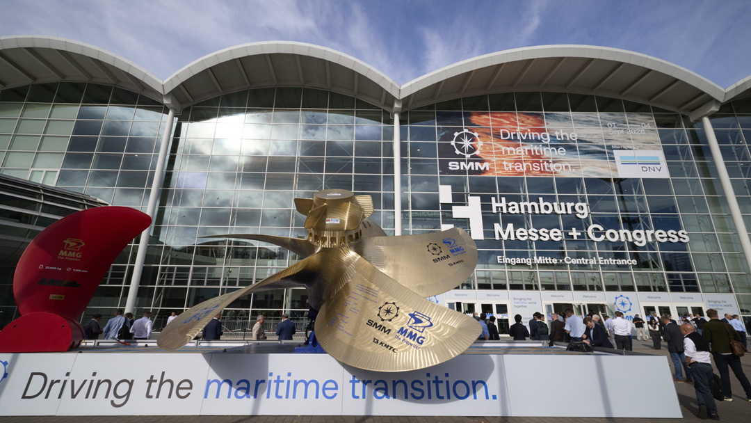 Blick auf den EIngangsbereich der Messehalle in Hamburg, MEnschen stehen Schlange im Vordergrund ist eine riesige Schiffsschraube zu sehen. Davor steht ein Schild auf dem steht "Driving the maritime future."