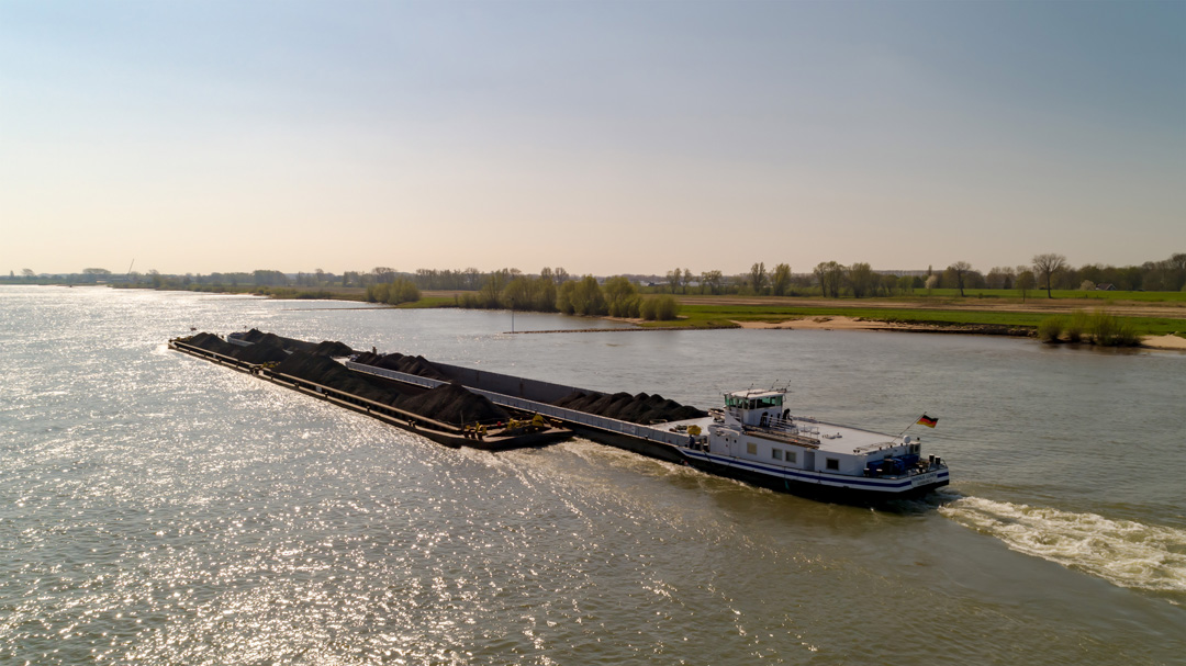 Rhenus integriert Binnenschifffahrt unter gemeinsamer Dachmarke Luftaufnahme eines Massengutfrachters der mit Kohle beladen ist auf einem Fluss